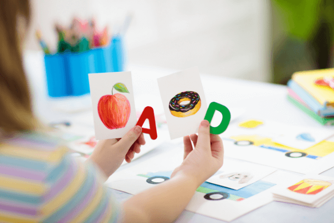 Child holding educational letter cards with apple and donut